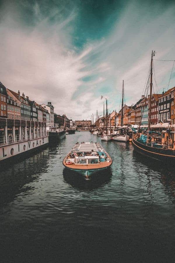 A canal boat gliding through Nyhavn, Copenhagen, with colourful historic buildings reflected in the water