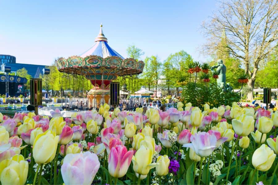 A vintage carousel surrounded by pink and yellow tulips in full bloom at Tivoli Gardens, Copenhagen — one of the best things to do in Denmark with kids