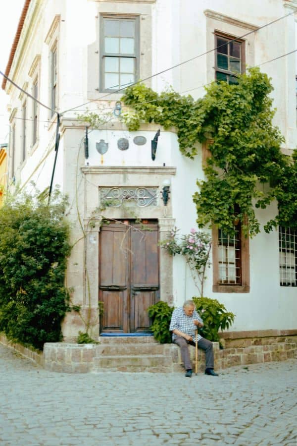 old man sitting in front of a whitewashed house in ayvalik balikesir turkey
