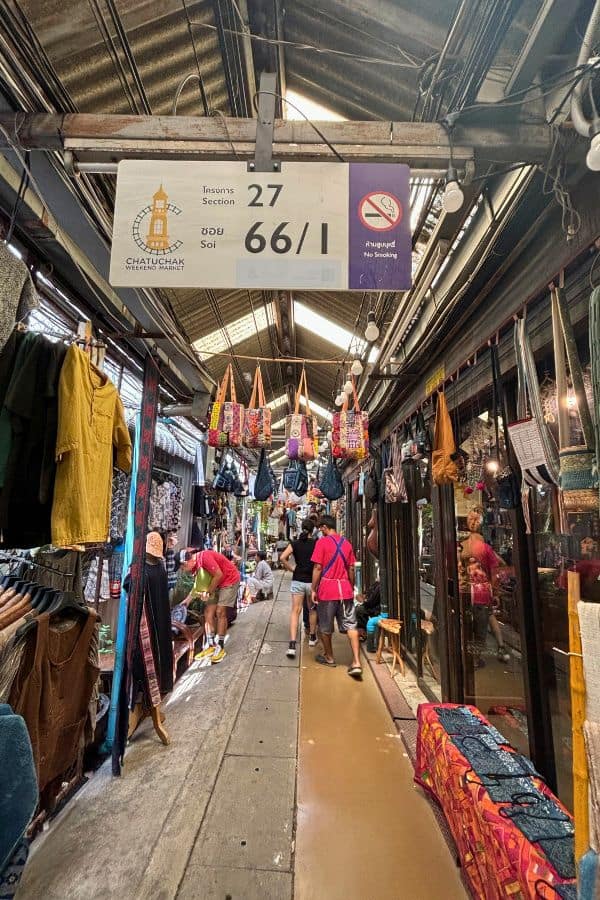 an alley at chatuchak weekend market in bangkok where shoppers browse through stalls selling colorful bags, clothing, and textiles 