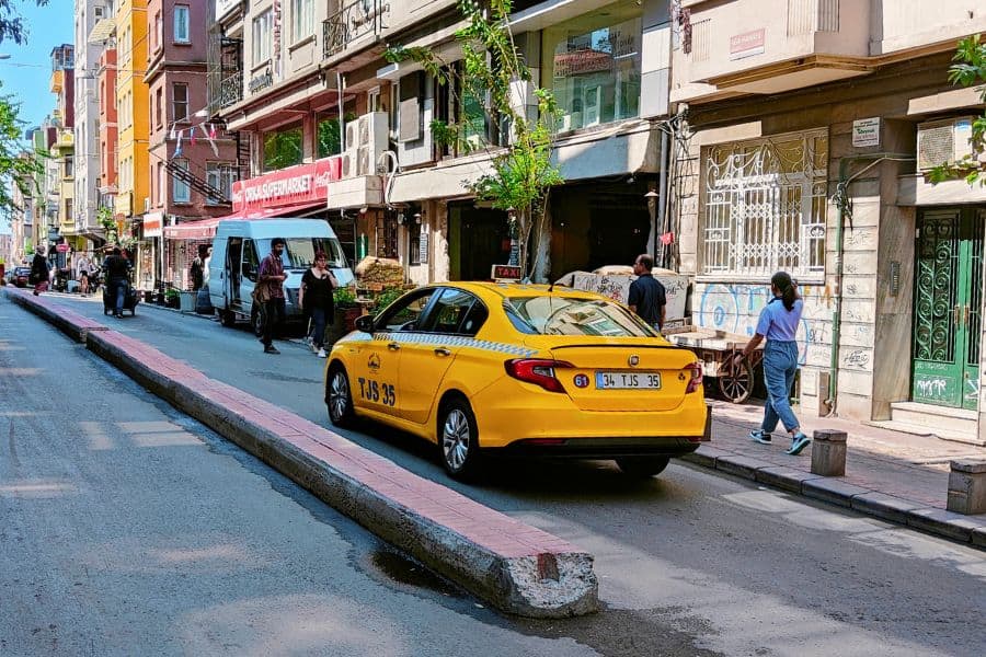 A few pedestrians are walking along and a yellow taxi is parked on a narrow street lined with multi-story buildings in beyoglu Istanbul