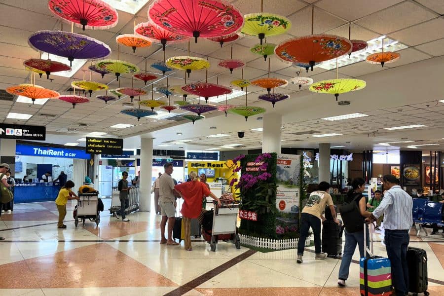 travelers moving around chiang mai international airport with a ceiling decorated with colorful traditional thai parasols
