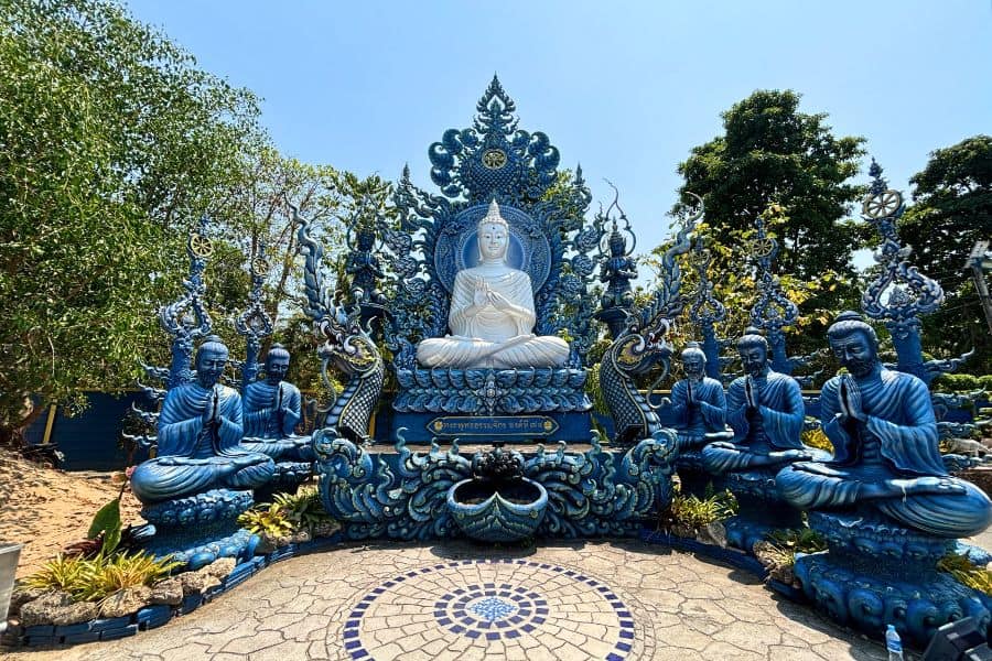 statue of a white buddha surrounded by six blue buddha statues in prayer at the blue temple in chiang rai