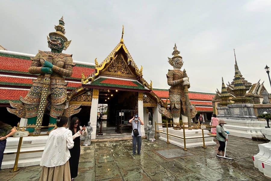 visitors taking photos near the towering guardian statues at wat phra kaew at grand palace in bangkok