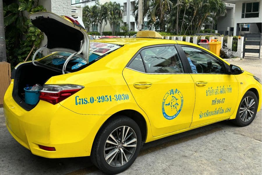 yellow taxi grab with open trunk showing water bottles and advertising signs in bangkok