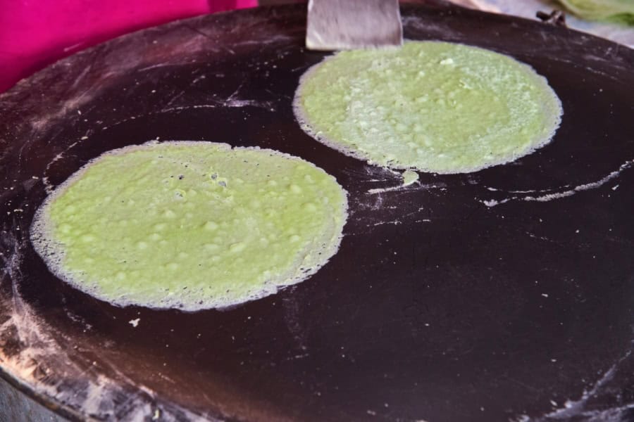freshly made green pandan-flavored roti sai mai being cooked on a hot griddle in ayutthaya, thailand, as part of the famous cotton candy roti dessert