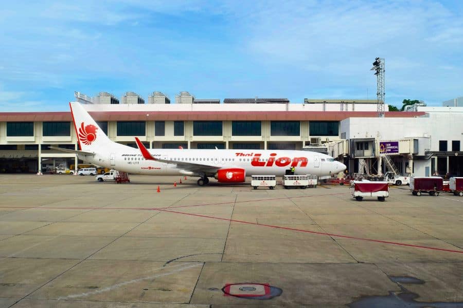 thai lion air plane parked at the airport gate with ground support vehicles and baggage carts around, ready for boarding