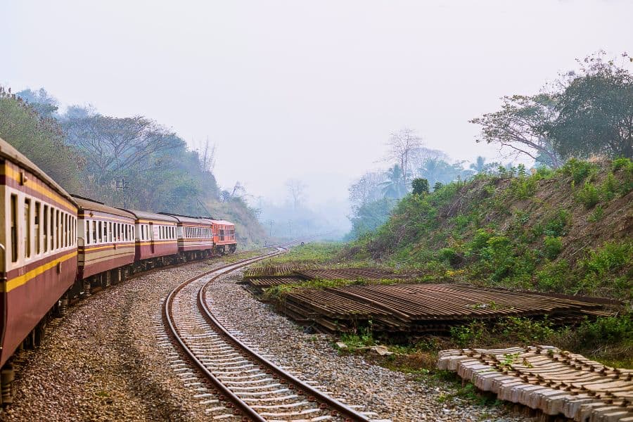 train traveling through lush countryside on a curved railway track, surrounded by greenery and misty hills
