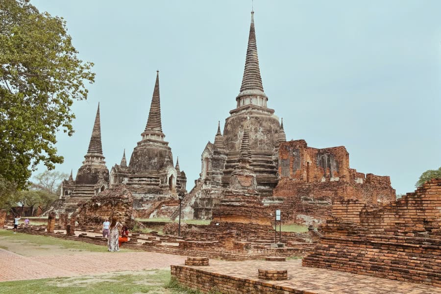 ancient temple ruins of wat phra si sanphet in ayutthaya, thailand, featuring three towering chedis surrounded by crumbling brick walls and scattered remains of the historic royal palace complex