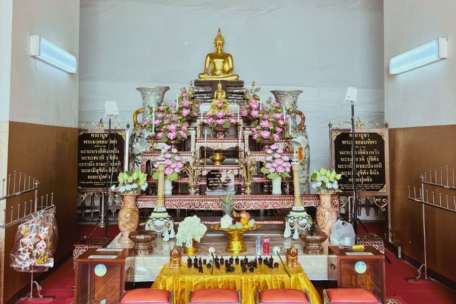 interior of wihan phra mongkhon bophit in ayutthaya, thailand, featuring a golden buddha statue on an ornate altar surrounded by floral offerings, candles, and religious artifacts
