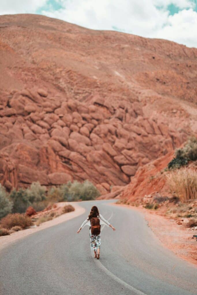 girl walking freely on a winding mountain road with reddish rock hills in the background, symbolizing travel and adventure