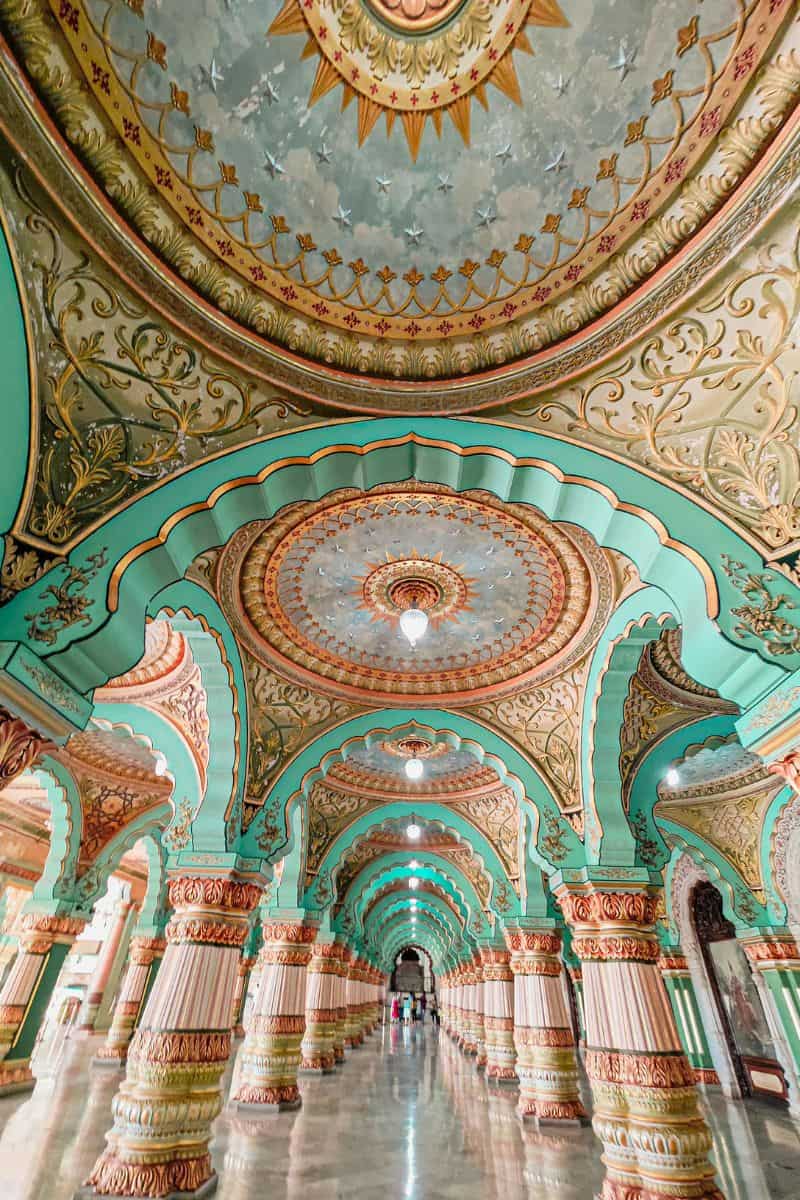 intricately designed arches and pillars in shades of mint green and gold inside the Mysore Palace in India, showcasing ornate carvings and a beautifully painted ceiling with star motifs and floral patterns