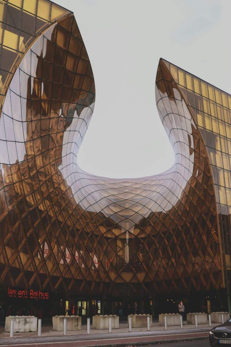 the striking modern architecture of Emporia shopping mall in Malmö, Sweden, featuring a dramatic curved glass facade with a golden hue and geometric pattern, reflecting surrounding buildings and the sky
