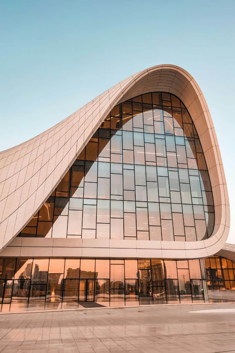 the futuristic, wave-like architecture of the Heydar Aliyev Center in Baku, Azerbaijan, designed by Zaha Hadid, with smooth curves, glass facades, and soft reflections under a clear blue sky