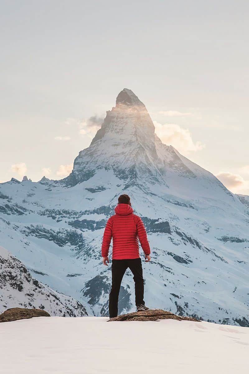 man in red jacket standing in front of iconic matterhorn mountain in zermatt switzerland