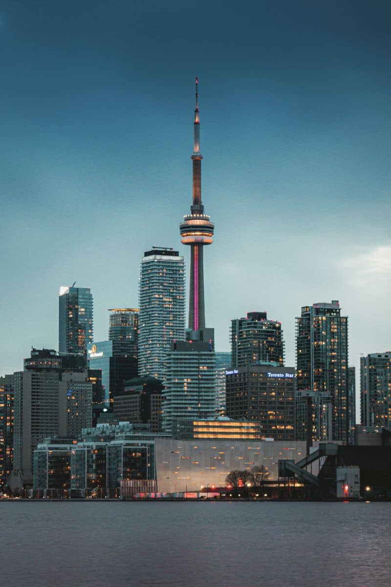 toronto skyline at dusk with the cn Tower illuminated, surrounded by modern high-rise buildings, viewed from across lake ontario