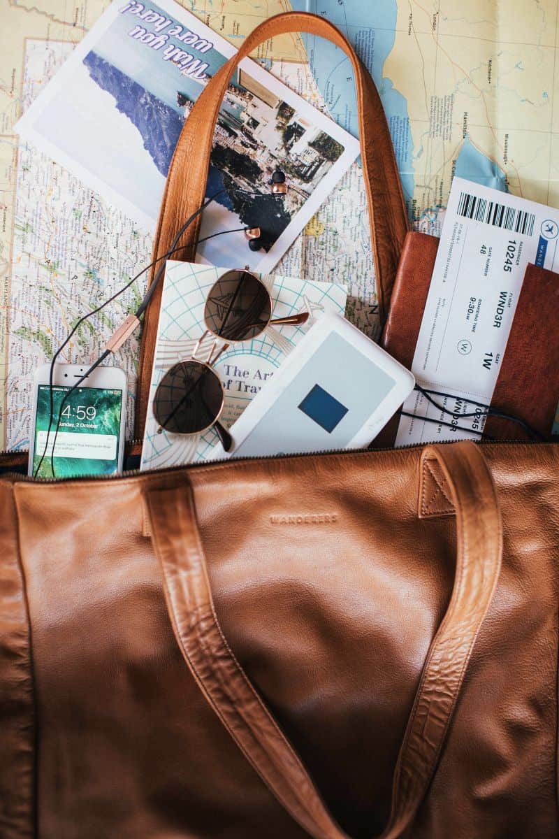brown leather travel bag with sunglasses, phone, passport, tickets, and travel book on a map
