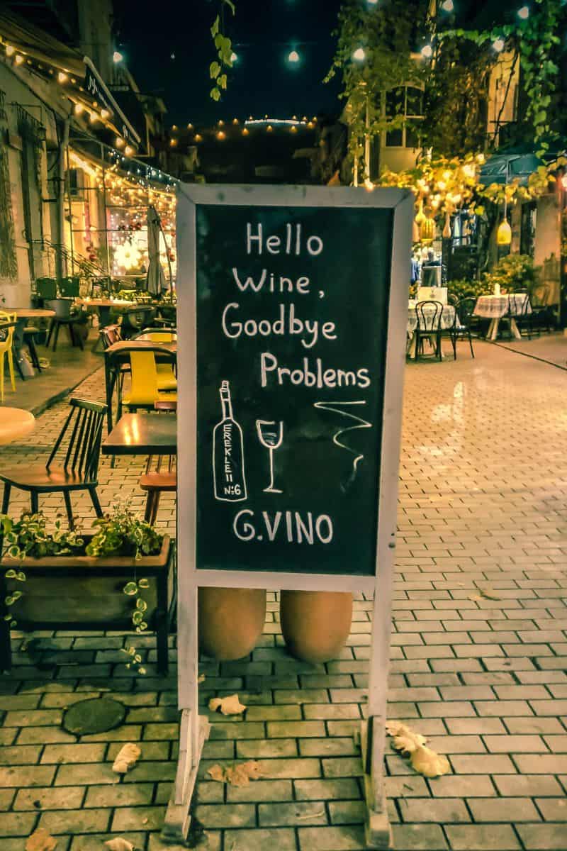 A glowing street sign at night outside G.Vino wine bar in Tbilisi, with cozy café lights and outdoor seating in the background