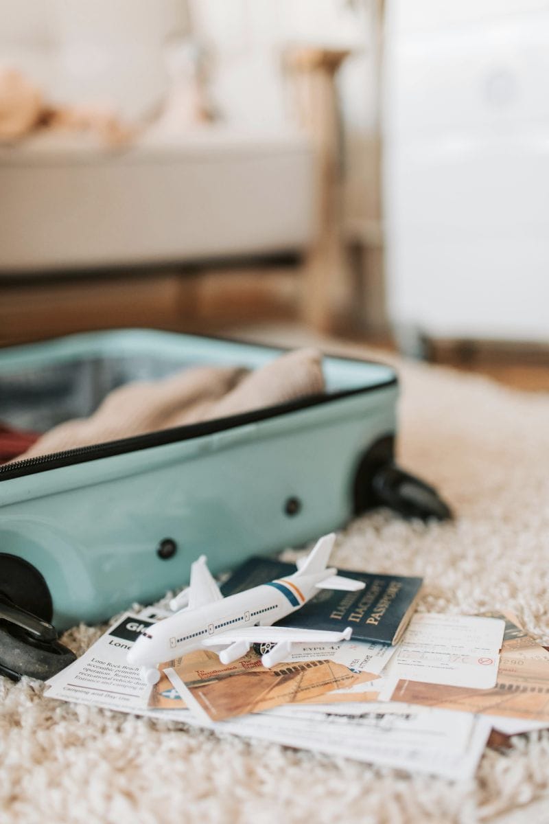 small blue suitcase on carpet with toy airplane passport and travel tickets