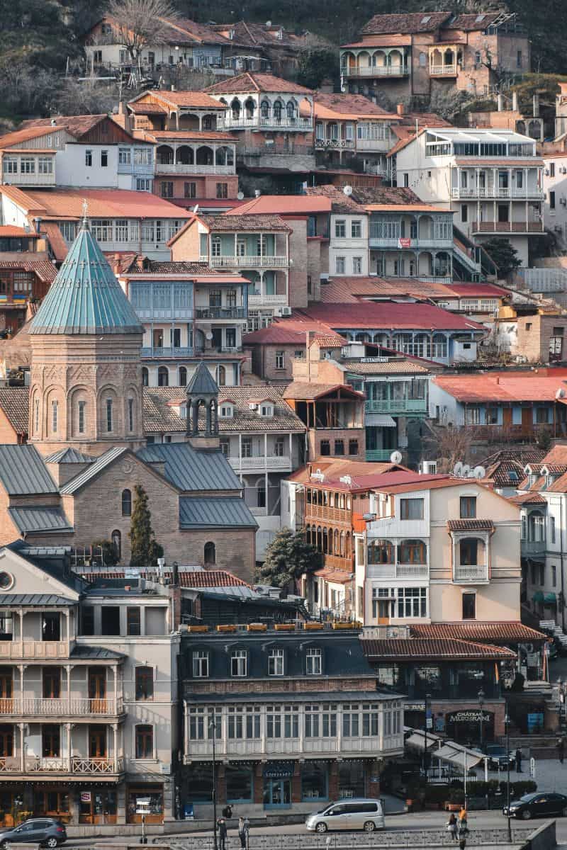 colorful traditional houses stacked on a hillside in old tbilisi with a domed church in the foreground and narrow streets below