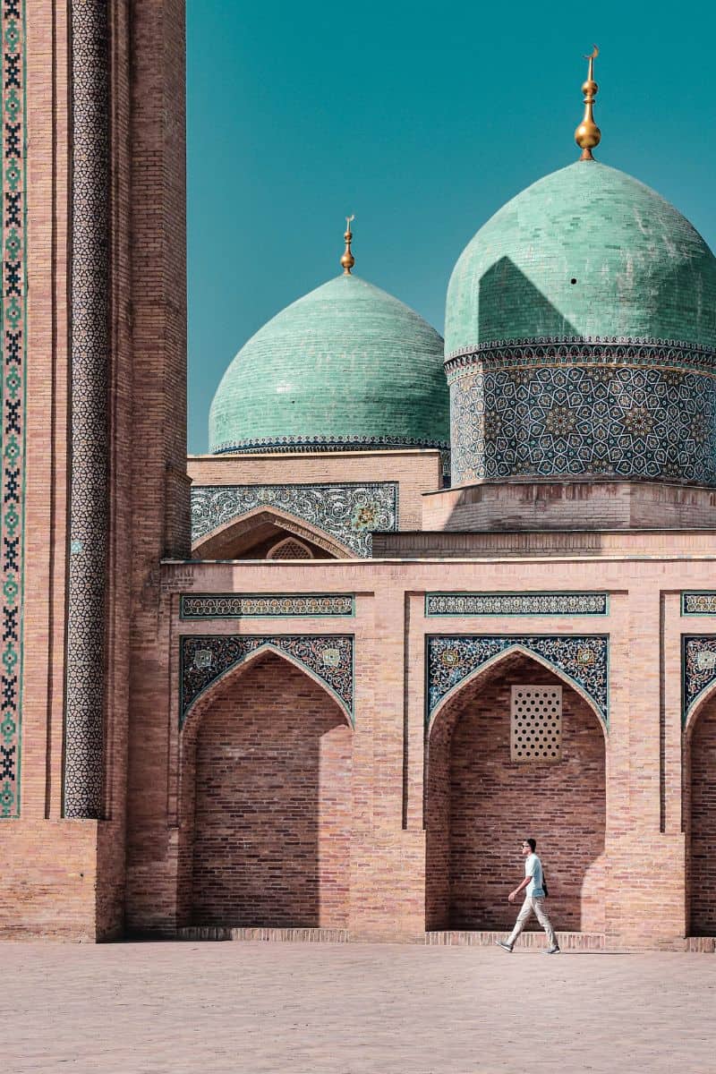 man walking past ancient mosque with turquoise domes in uzbekistan