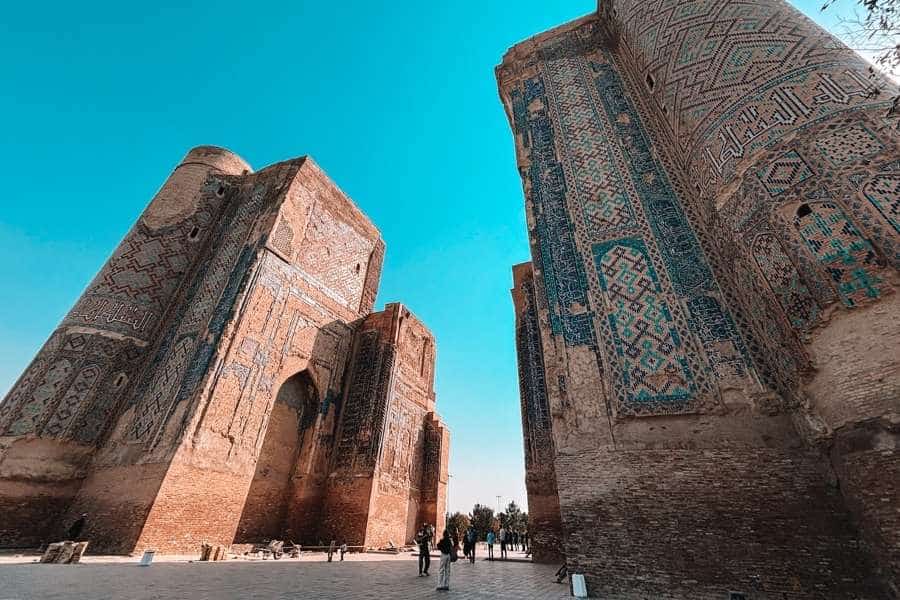 ruins of ak-saray palace in shahrisabz showing massive brick walls with faded turquoise tilework and towering arched facades against a blue sky