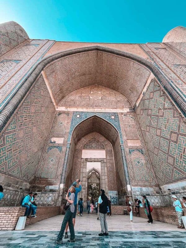inside the grand arch of bibi khanum mosque showing detailed geometric tilework and people standing beneath the massive portal