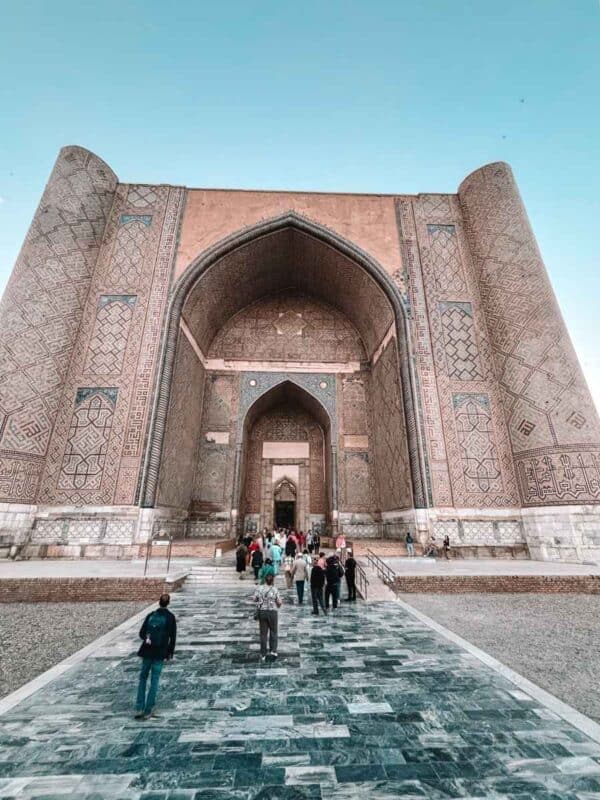 bibi khanum mosque main entrance in samarkand with towering tiled arch and visitors walking up marble steps
