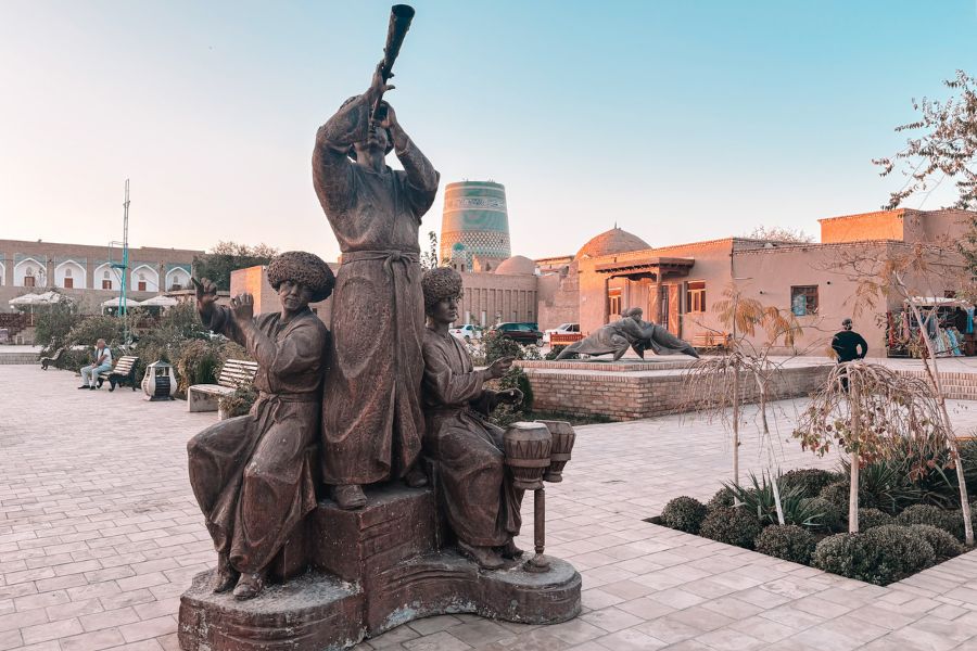 bronze statue of khiva musicians playing traditional instruments in itchan kala with kalta minor minaret in background