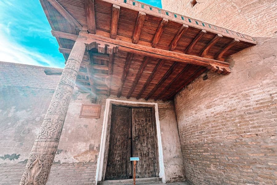 entrance of juma mosque khiva with carved wooden column and old wooden doors under a shaded porch
