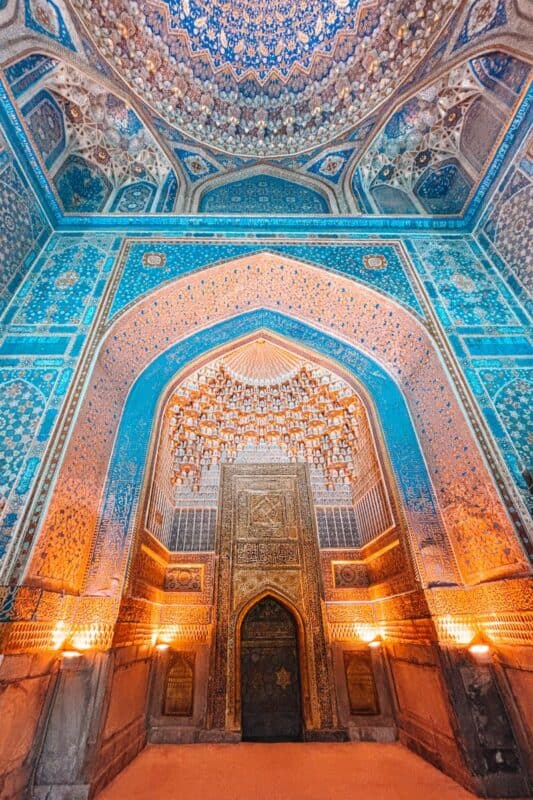 intricate interior of gur-e-amir mausoleum in samarkand, decorated with blue and gold mosaics, arched patterns, and muqarnas ceiling glowing under soft lights