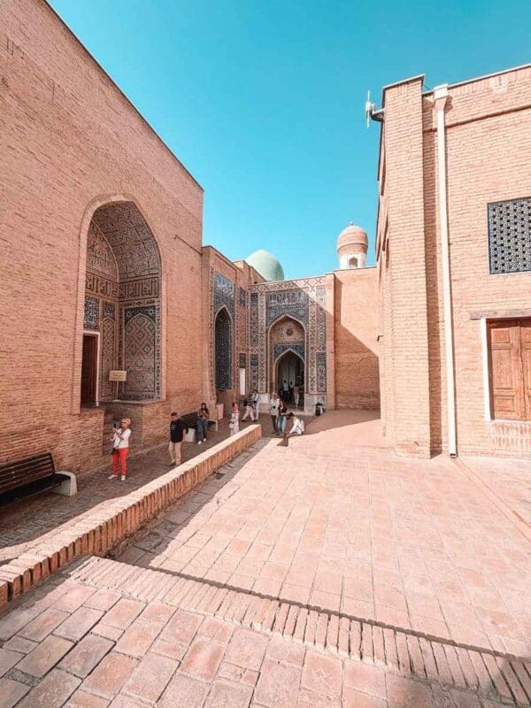 inner courtyard of shakhi zinda ensemble with brick madrasah buildings and visitors walking through