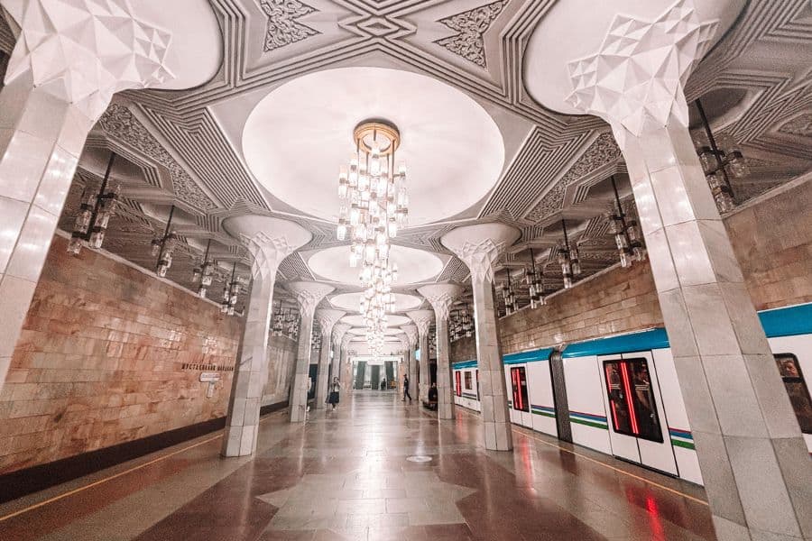 mustaqillik maydoni station in tashkent metro, beautifully designed with marble columns, chandeliers, and ornate ceiling details, featuring a train stopped at the platform