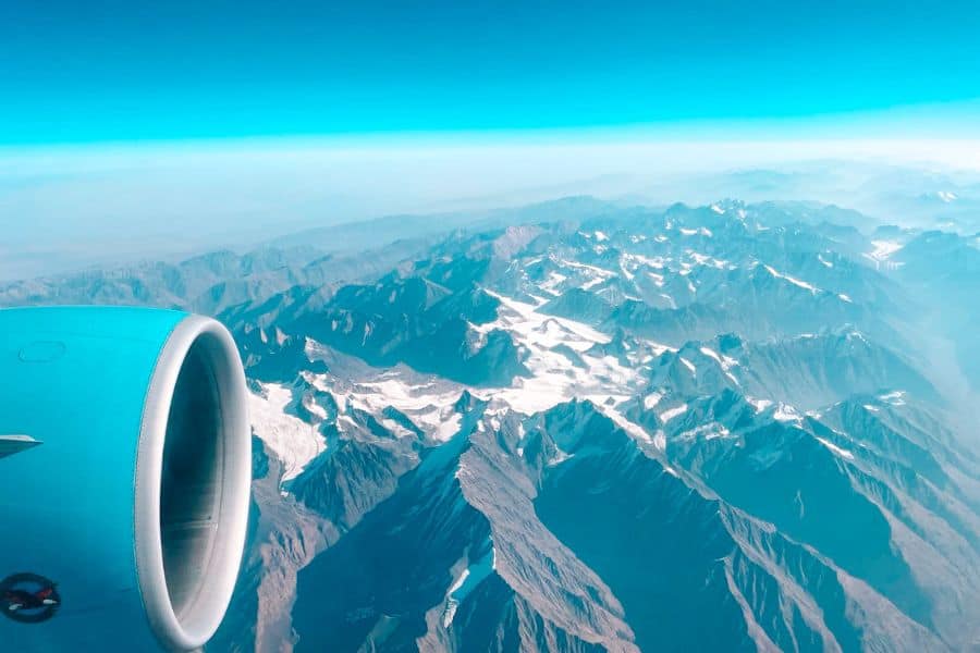 aerial view of the pamir, hindu kush, tian shan, and karakoram mountain ranges seen from a plane window on the tashkent to delhi flight, with snow-covered peaks and deep valleys stretching below a clear blue sky