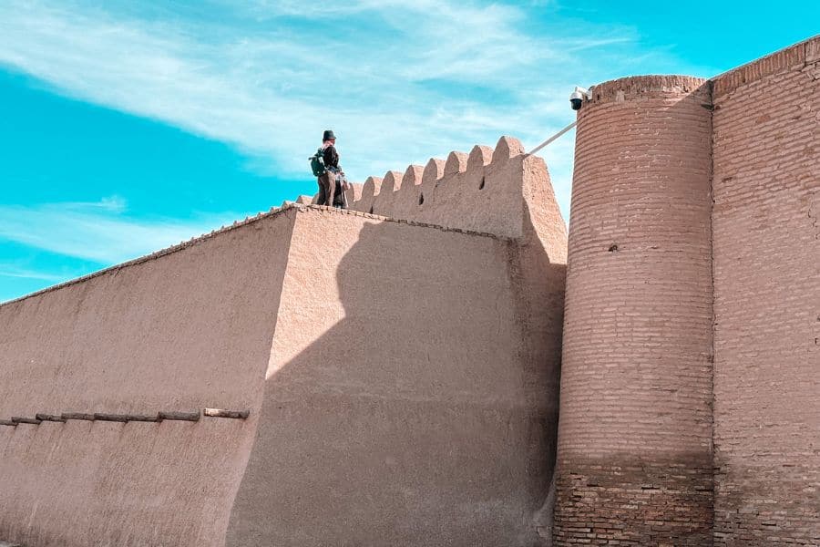 person standing on itchan kala city walls in khiva with mud brick fortifications and watchtower