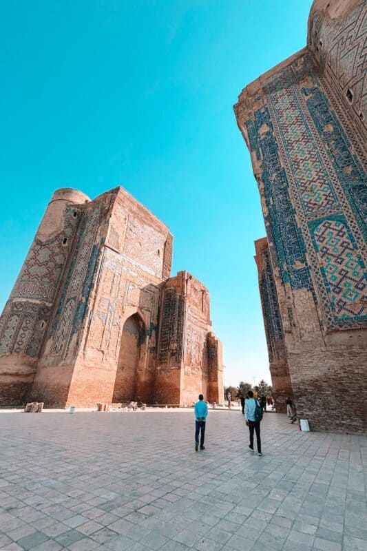 ruins of ak-saray palace in shahrisabz, uzbekistan, with towering brick walls covered in faded turquoise tilework under a clear blue sky