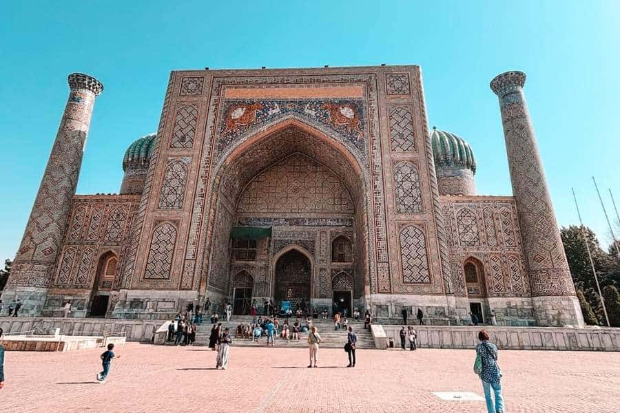 sher-dor madrasah at registan square in samarkand with animal mosaic above the main iwan and visitors in the courtyard
