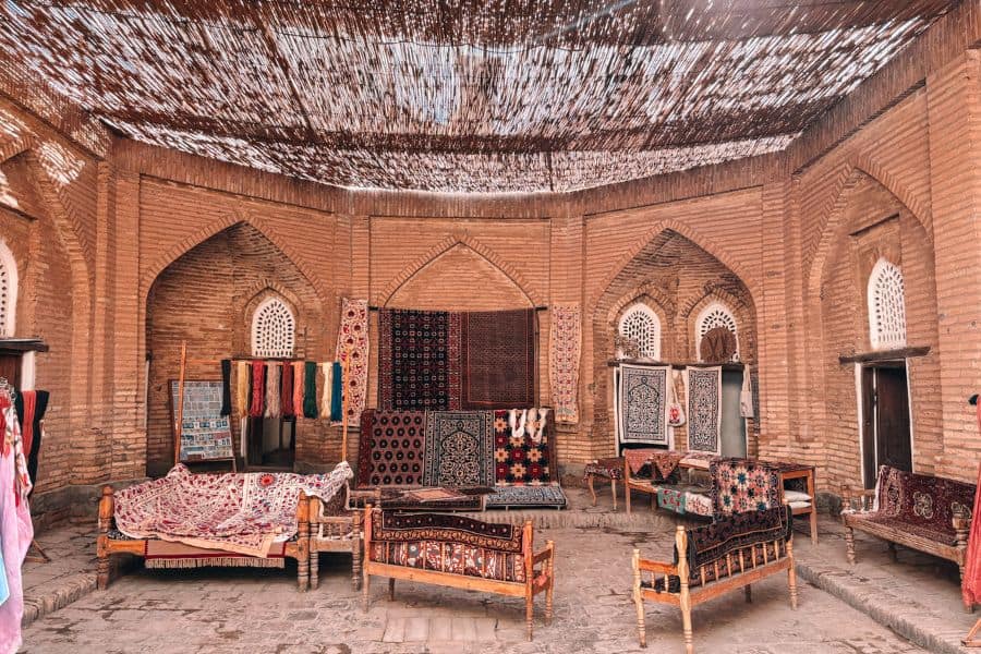 silk carpet workshop in itchan kala khiva with carpets wooden furniture and textile displays under shaded roof