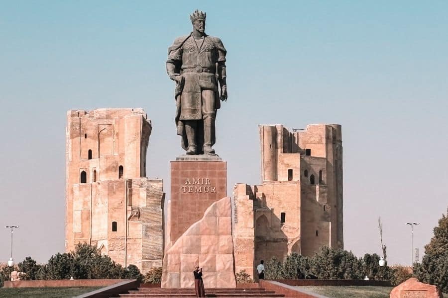 statue of amir timur standing on a stone pedestal with the ruins of ak-saray palace visible behind, shahrisabz, uzbekistan