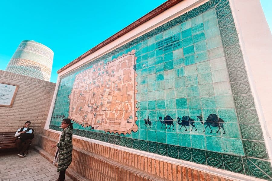 tiled map mural of itchan kala in khiva, uzbekistan, showing ancient city layout with camel caravan design and kalta minor minaret visible in the background