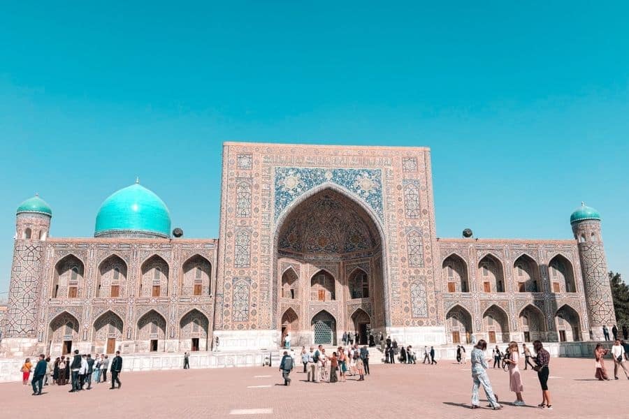 tilya-kori madrasah at registan square in samarkand with turquoise dome and visitors