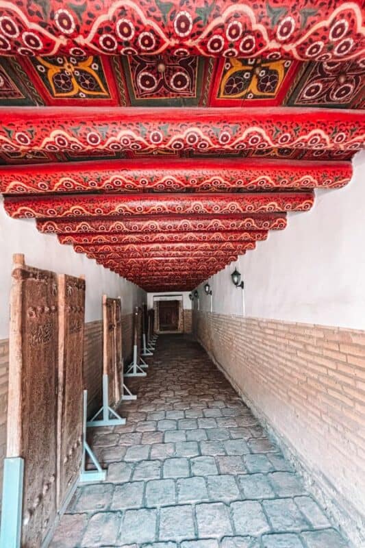 interior corridor of tosh hovli palace khiva with red painted wooden ceiling and historic carved doors