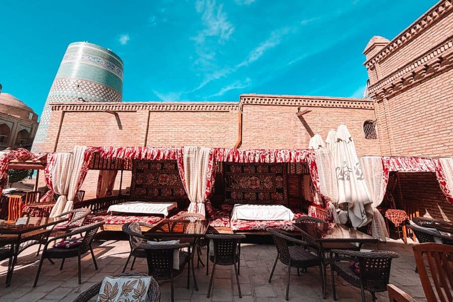 traditional chaikhana seating in itchan kala khiva with tapchan daybeds under canopy and kalta minor minaret in background