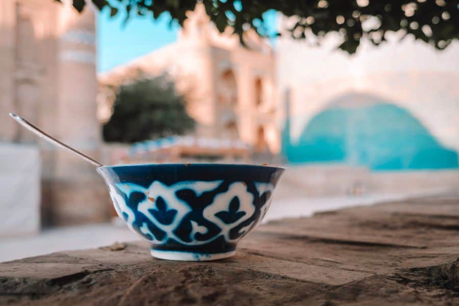 traditional uzbek ceramic bowl on wooden table in khiva with historic architecture blurred in background