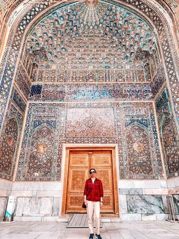 travel melodies author blogger standing in front of ornate tiled iwan inside ulugh beg madrasah at registan square