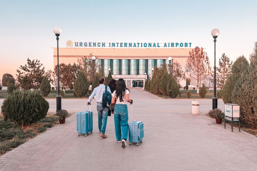 me clicking hubby and mini-me walking toward urgench international airport in uzbekistan with matching blue suitcases at sunset, ready for our evening flight back to tashkent