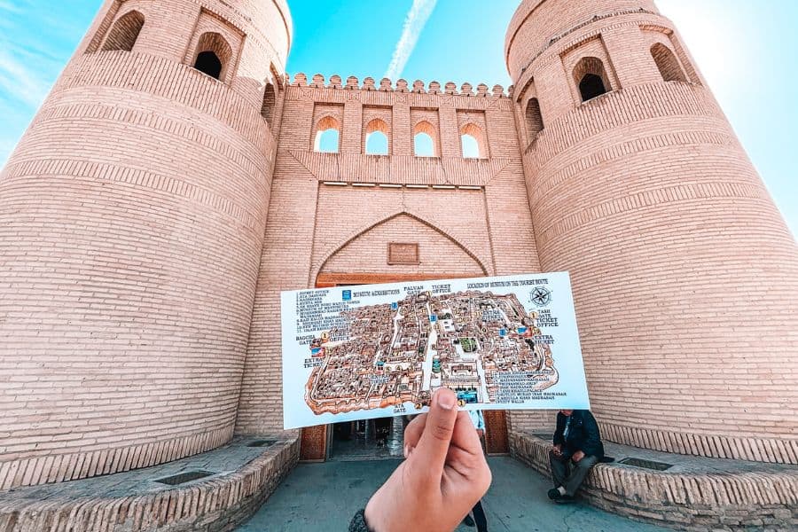 and holding a map in front of ata darwaza west gate of itchan kala khiva with twin mud brick towers
