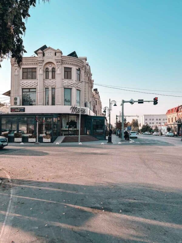 neoclassical corner building in university boulevard in samarkand city center with ornate white facade, tall arched windows, and a street-level café mone at a traffic intersection