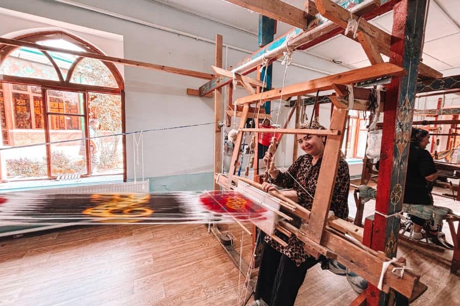 woman weaving traditional ikat silk fabric on a wooden loom at yodgorlik silk factory in margilan, uzbekistan