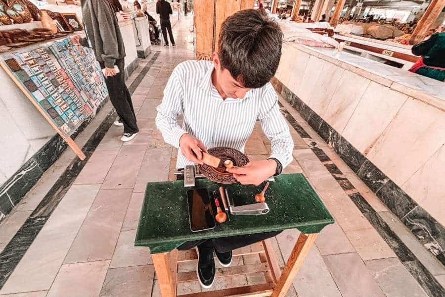 young artisan carving a decorative wooden plate at siyob market